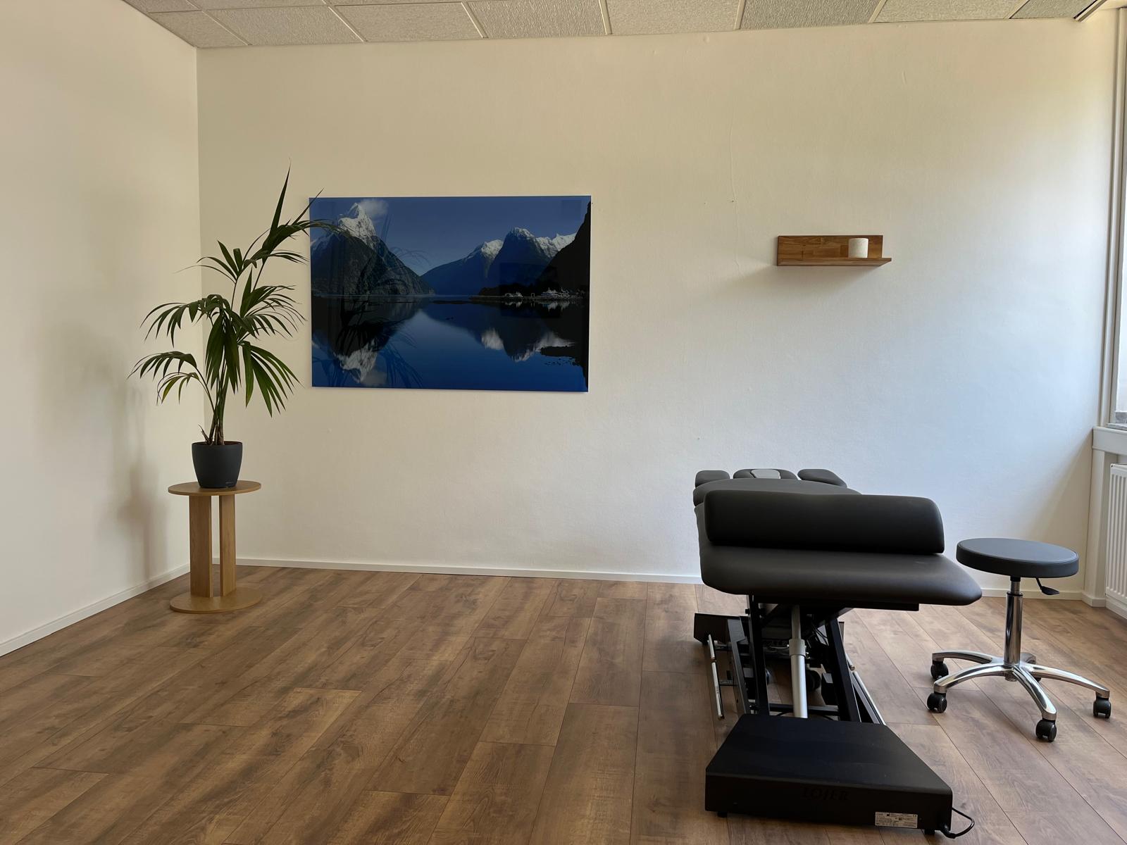 Behandlungsraum mit schwarzer Therapieliege und Bergmotiv